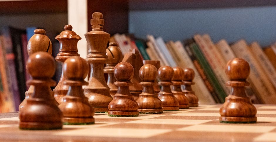 Wooden chess pieces set up on a chessboard with books in the background. Ideal for strategic and intellectual themes.