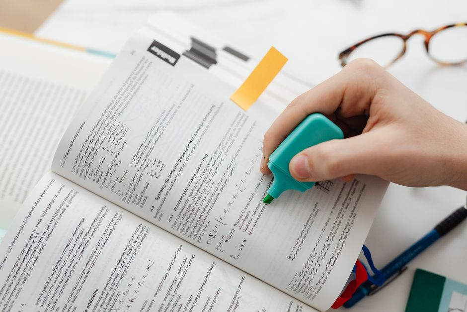 Close-up of a hand using a highlighter on an open textbook, focusing on key information.